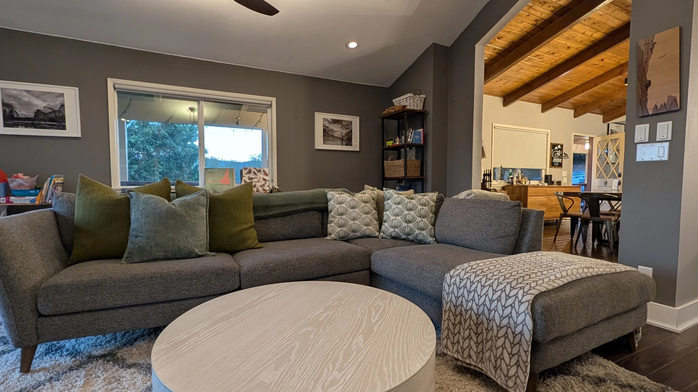 Grey sectional around a round coffee table, open to the dining room