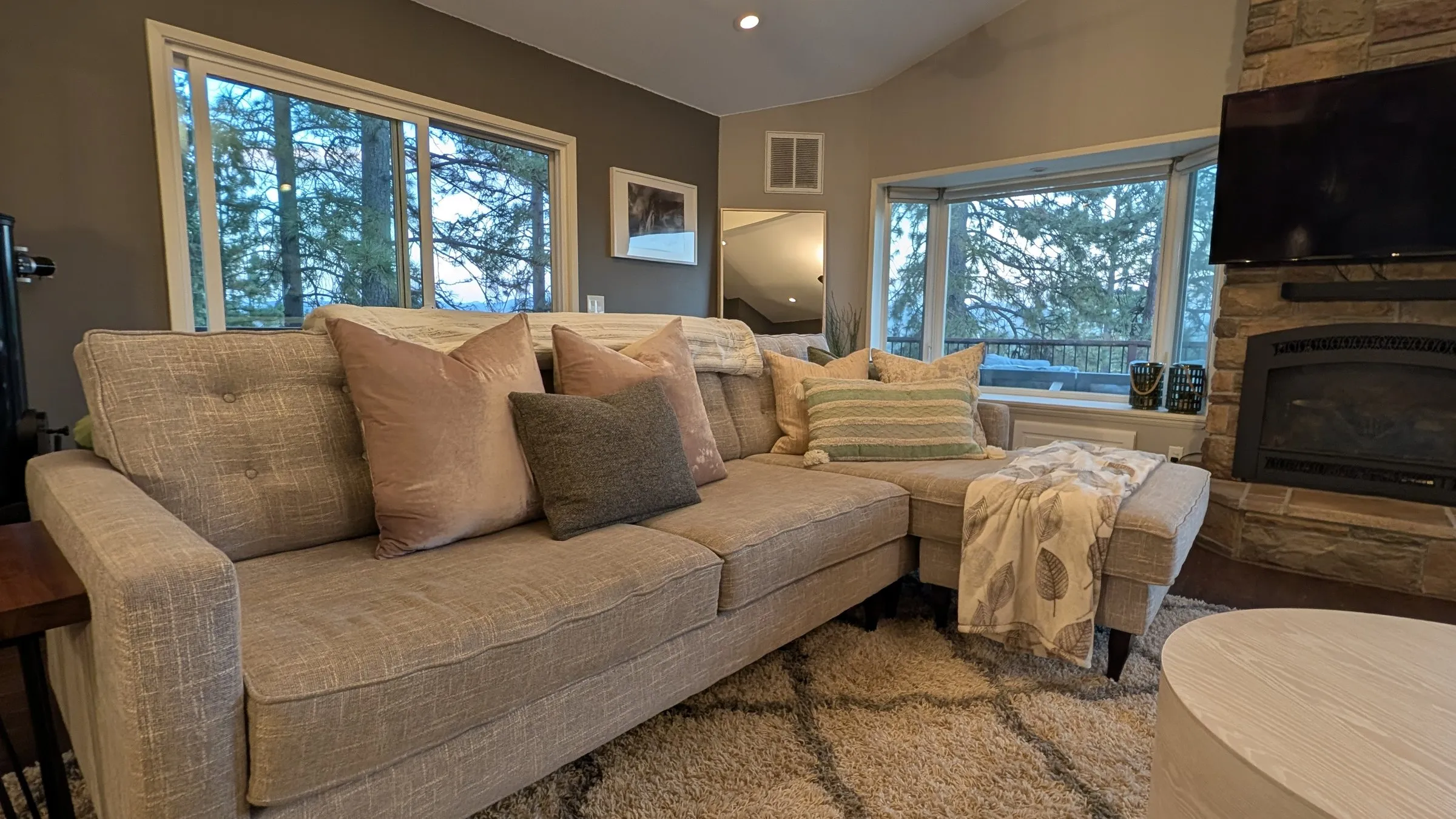 Living room sectional facing the stone fireplace, windows into the pines